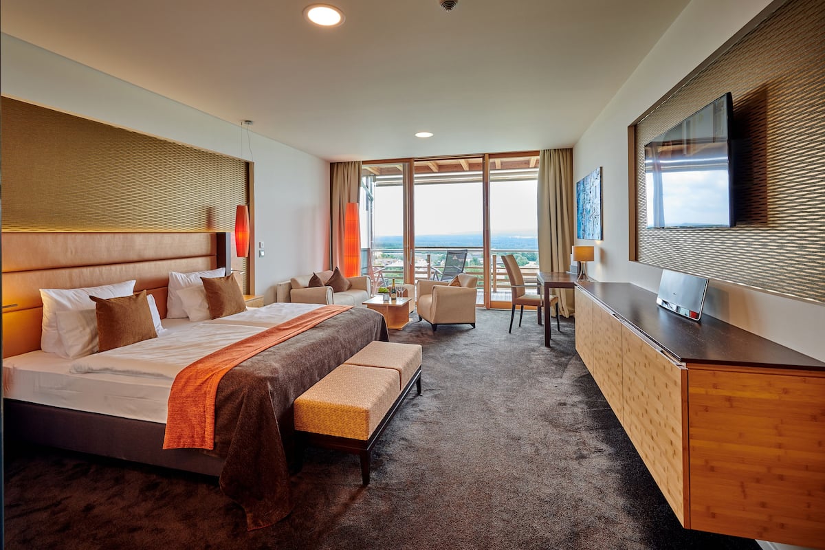 A hotel room with a large bed, a desk, a chair, and a TV on the wall.