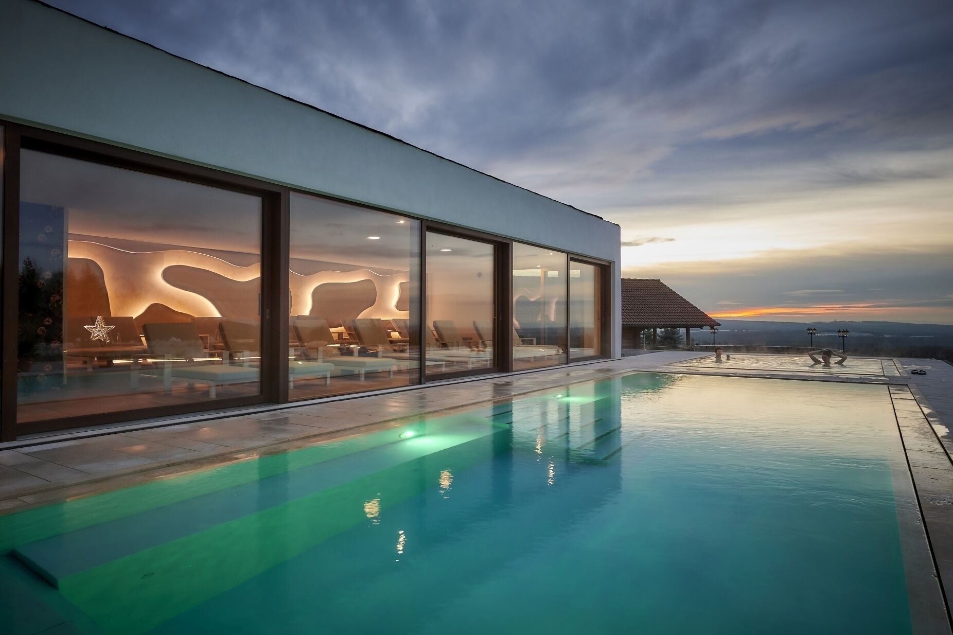 Un edificio moderno con fachada de vidrio, piscina y vistas al atardecer.