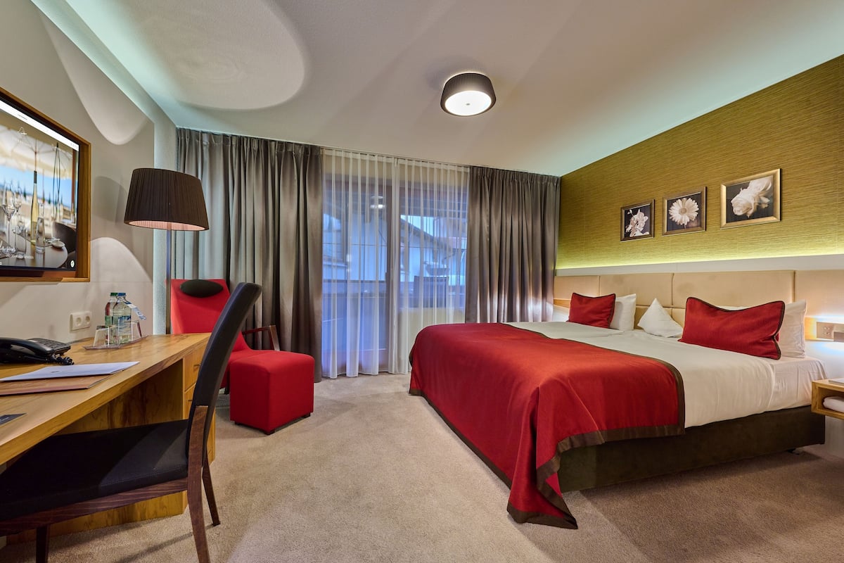 A hotel room with a large bed, a desk, a chair, a TV, and a window with curtains.