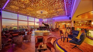 Een ruime lounge met een vleugelpiano, comfortabele zithoek en grote ramen met uitzicht op de stad.