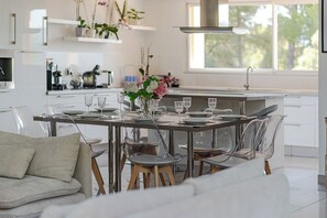 Une cuisine moderne avec un coin repas, comprenant un îlot central, des chaises transparentes et un vase de fleurs.