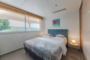 Une chambre à coucher avec un grand lit, une tête de lit, une table de chevet avec une lampe, une fenêtre avec des stores et un tableau au mur.