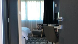 Una habitación de hotel moderna con cama, escritorio, silla y un ventanal con cortinas.