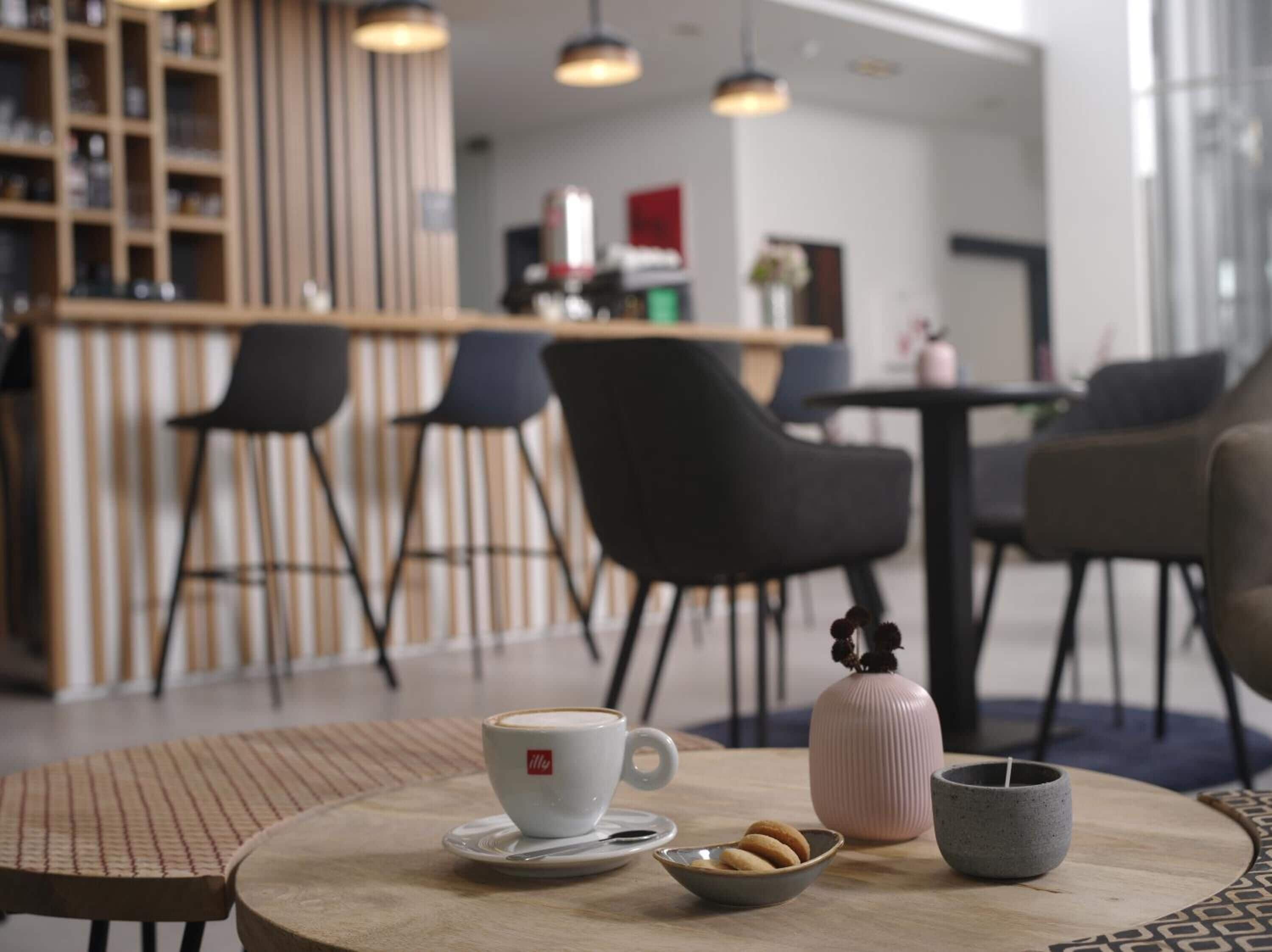 A modern cafe with a wooden counter, black chairs, and a round table with a cup, cookies, and a candle.