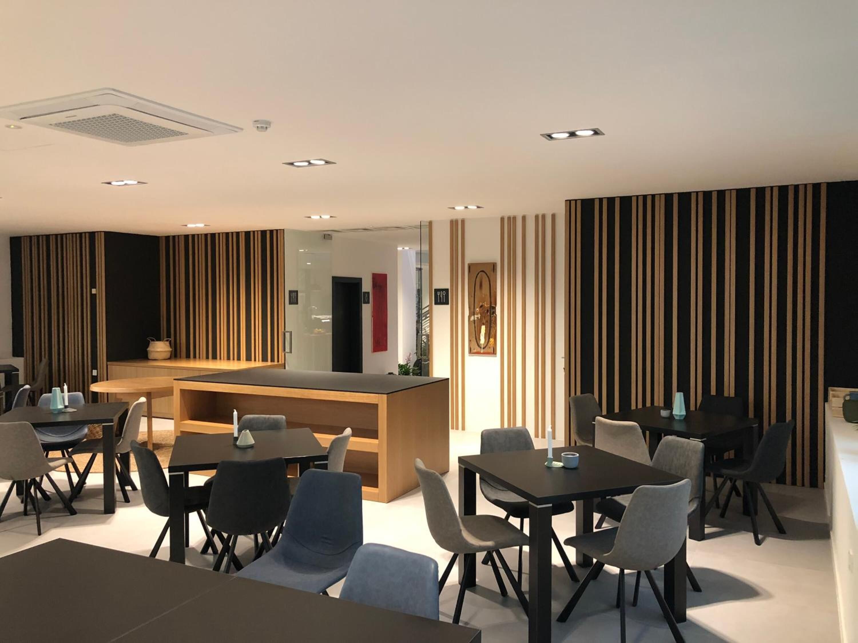 Un moderno vestíbulo de hotel con una recepción, varias zonas de estar y una pared decorativa con rayas verticales.