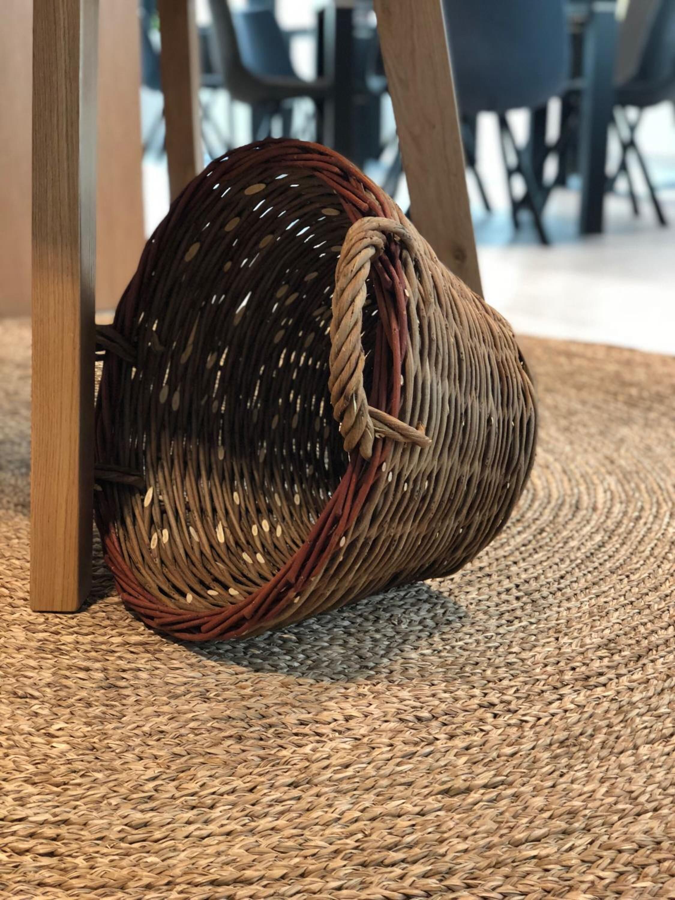 A woven basket with a rope handle, placed on a woven mat.