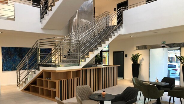 Un vestíbulo moderno con una escalera central, un área de descanso y una recepción.