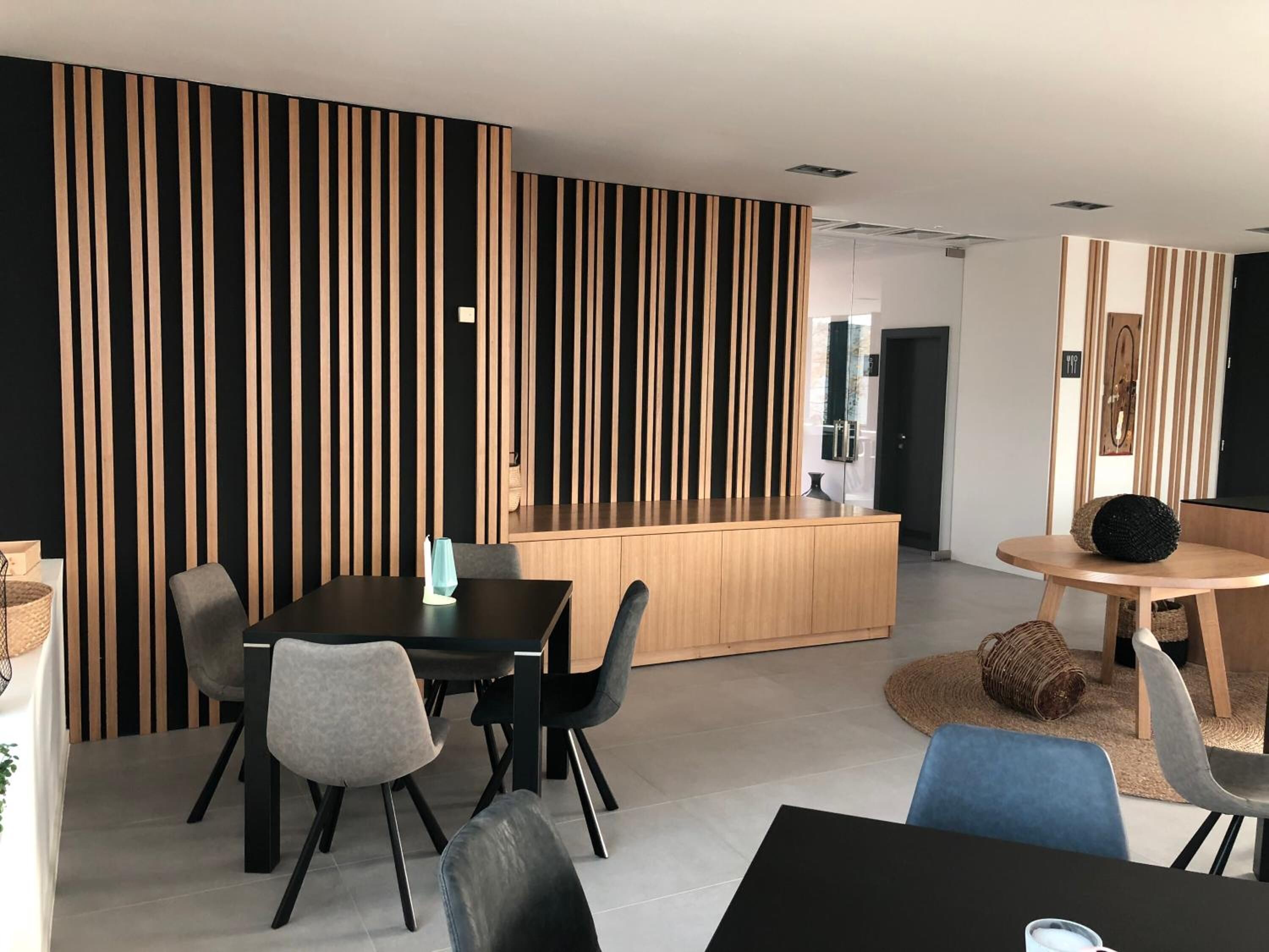 A modern dining area with a black table, grey chairs, and a wooden reception desk.