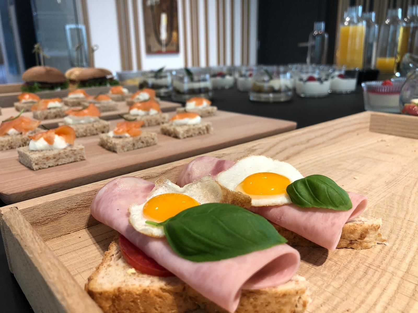 Una mesa de buffet con diversos alimentos, entre ellos sándwiches, huevos y salmón ahumado.