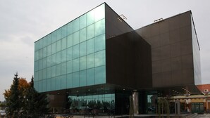 Un edificio moderno con fachada de vidrio, zona de estar al aire libre y una escalera que conduce a la entrada.