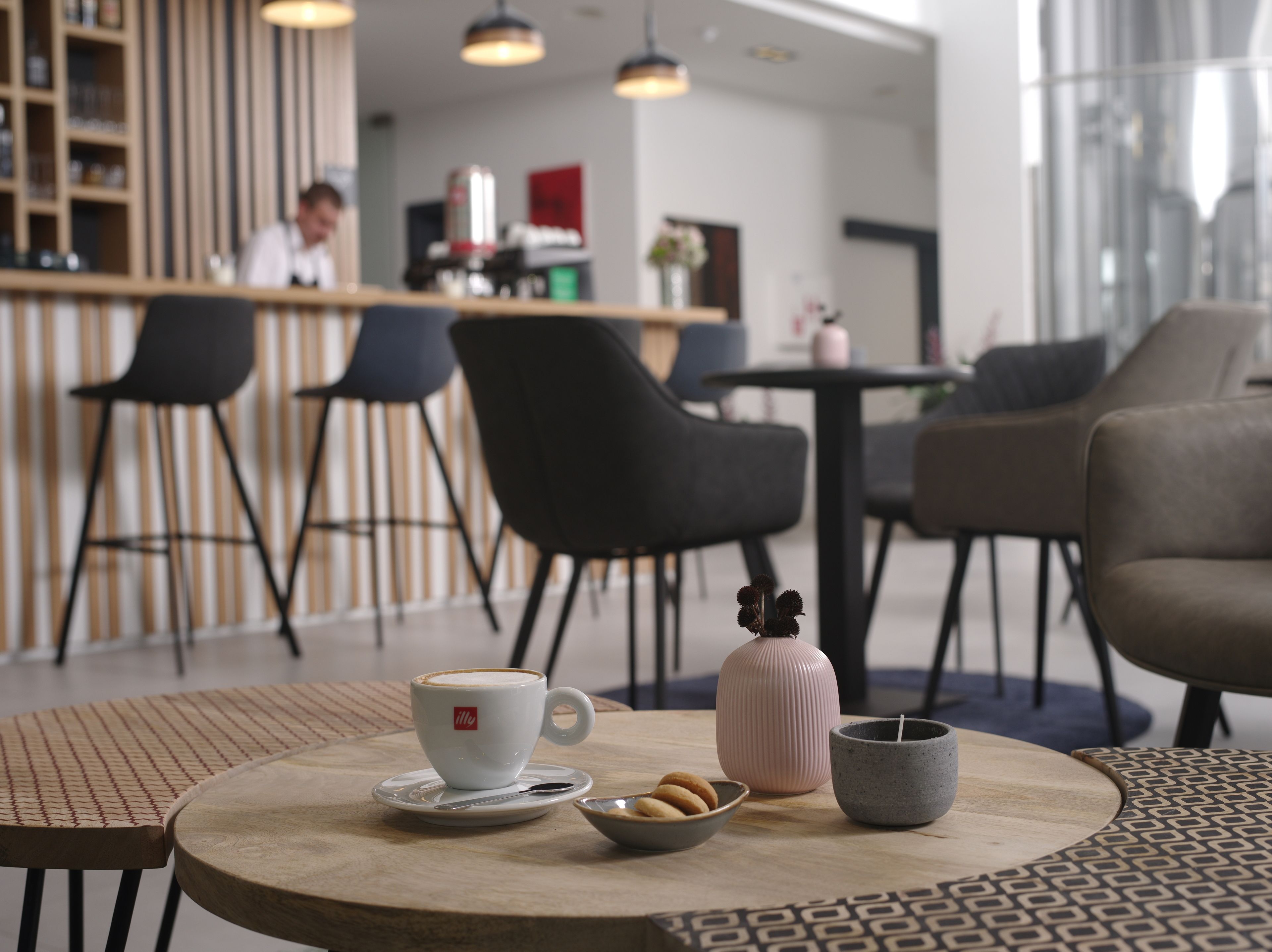 A modern cafe interior with a bar area, seating arrangements, and a coffee table with a cup, cookies, and a candle.