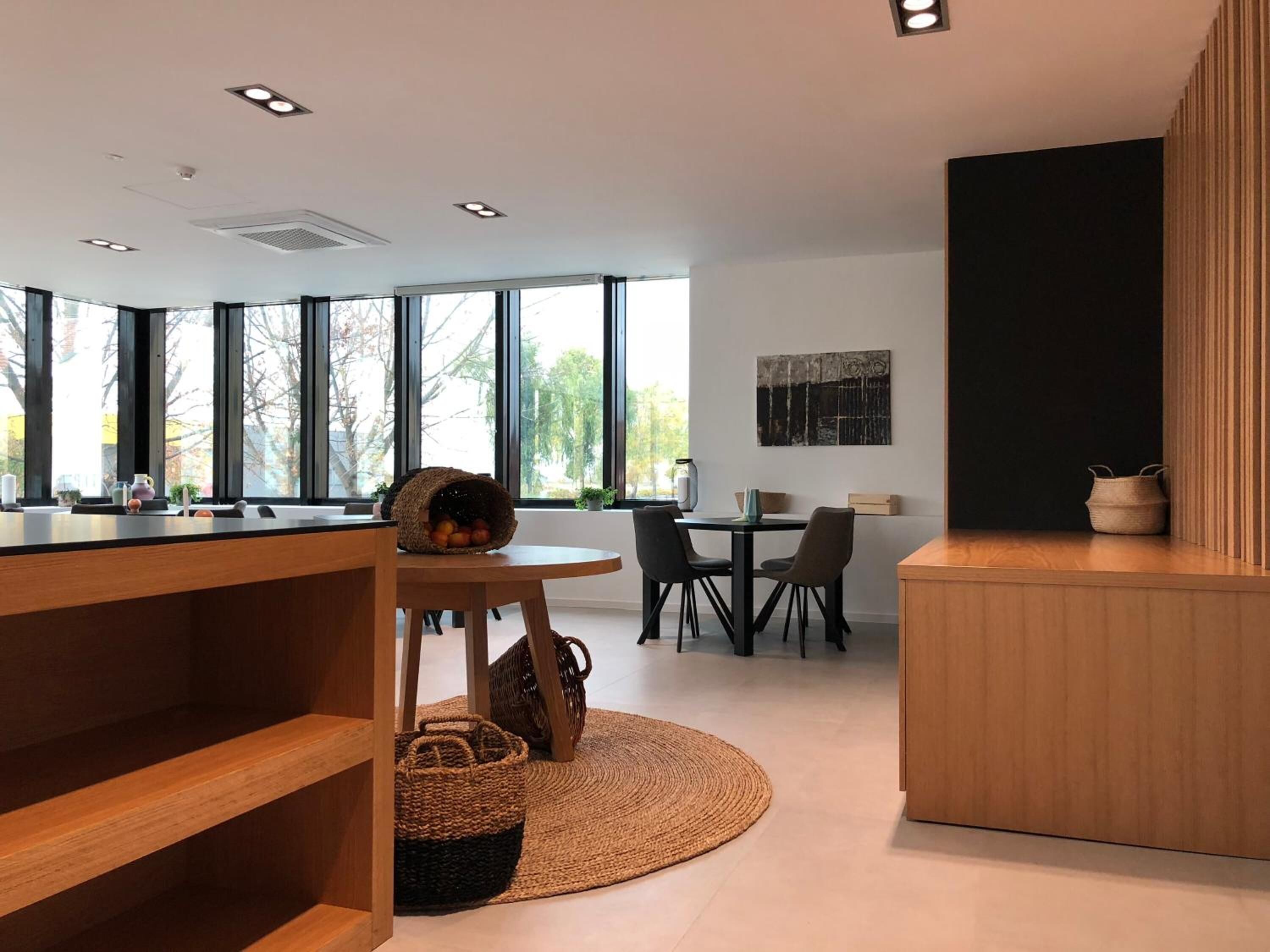 A modern kitchen with a wooden counter, a round dining table with chairs, and a large window providing natural light.