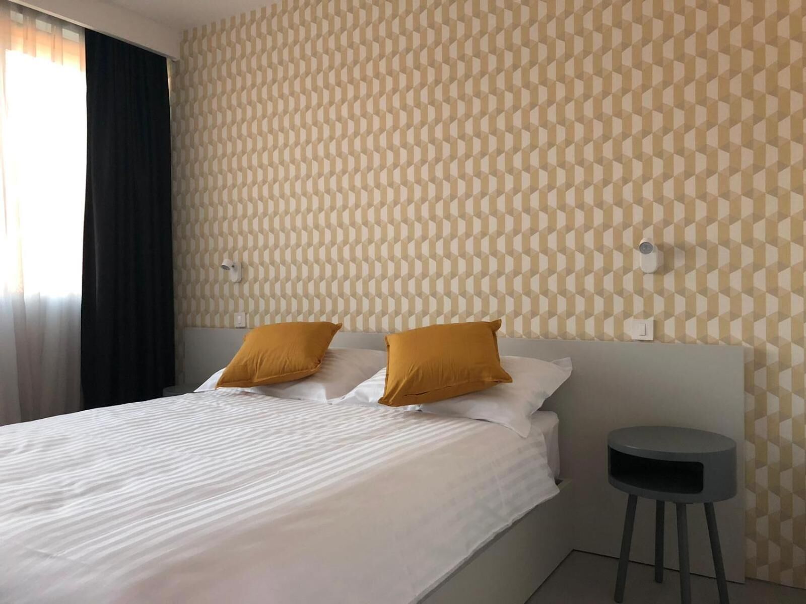 Hotelkamer met een bed, twee kussens, een nachtkastje en een muur met een geometrisch patroon.