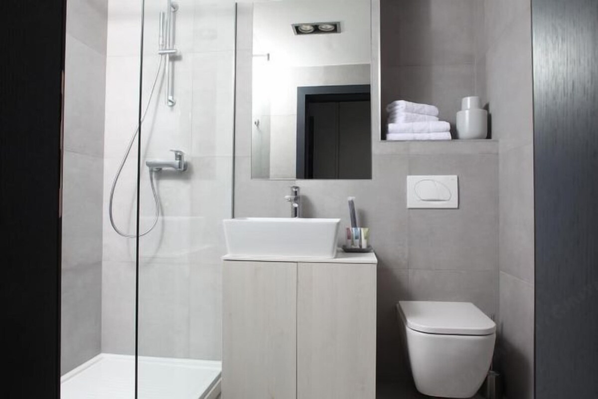 A modern bathroom with a glass-enclosed shower, a white sink, a toilet, and a mirror above the sink.
