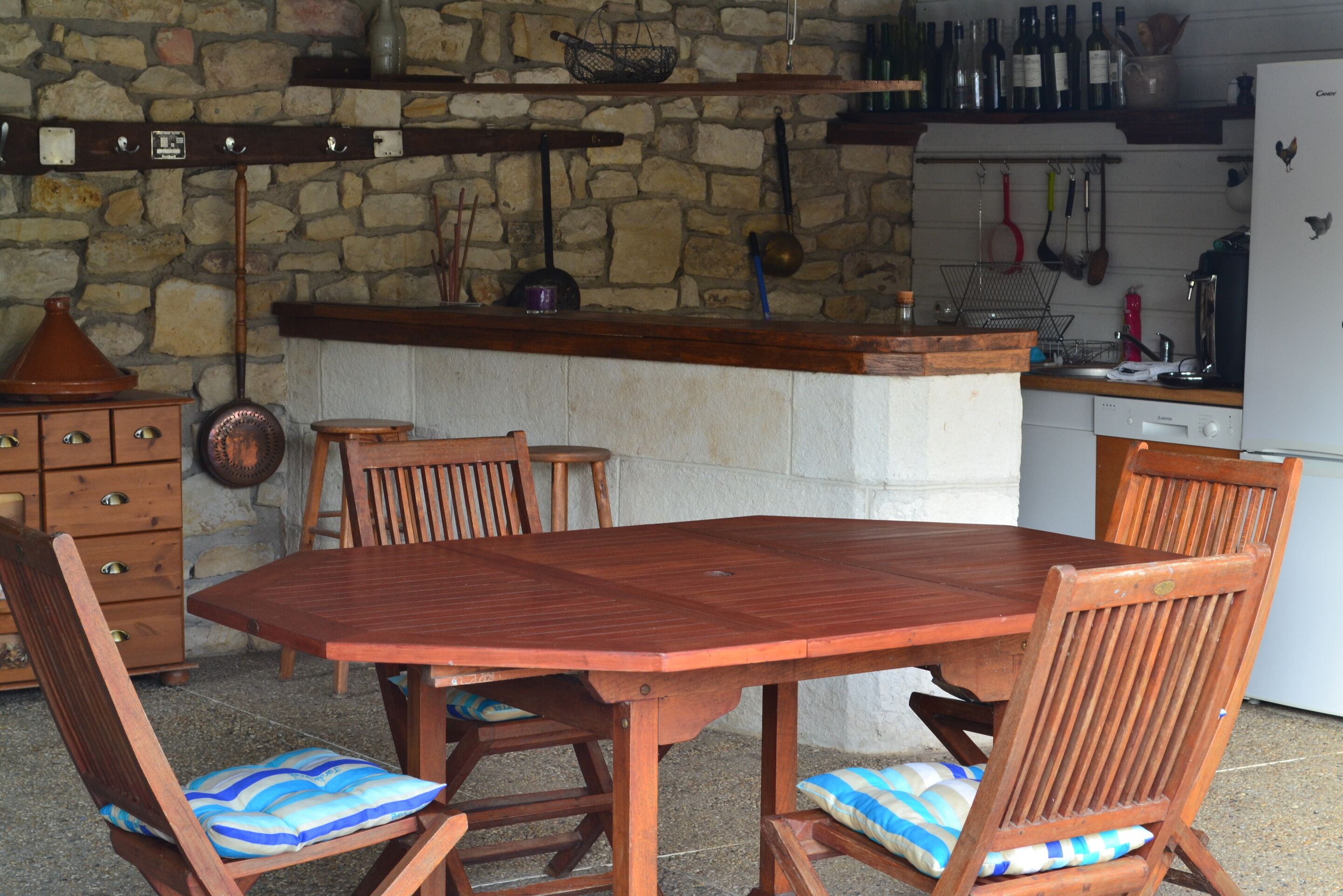 A wooden dining table with chairs, a stone wall, and kitchen utensils hanging on the wall.
