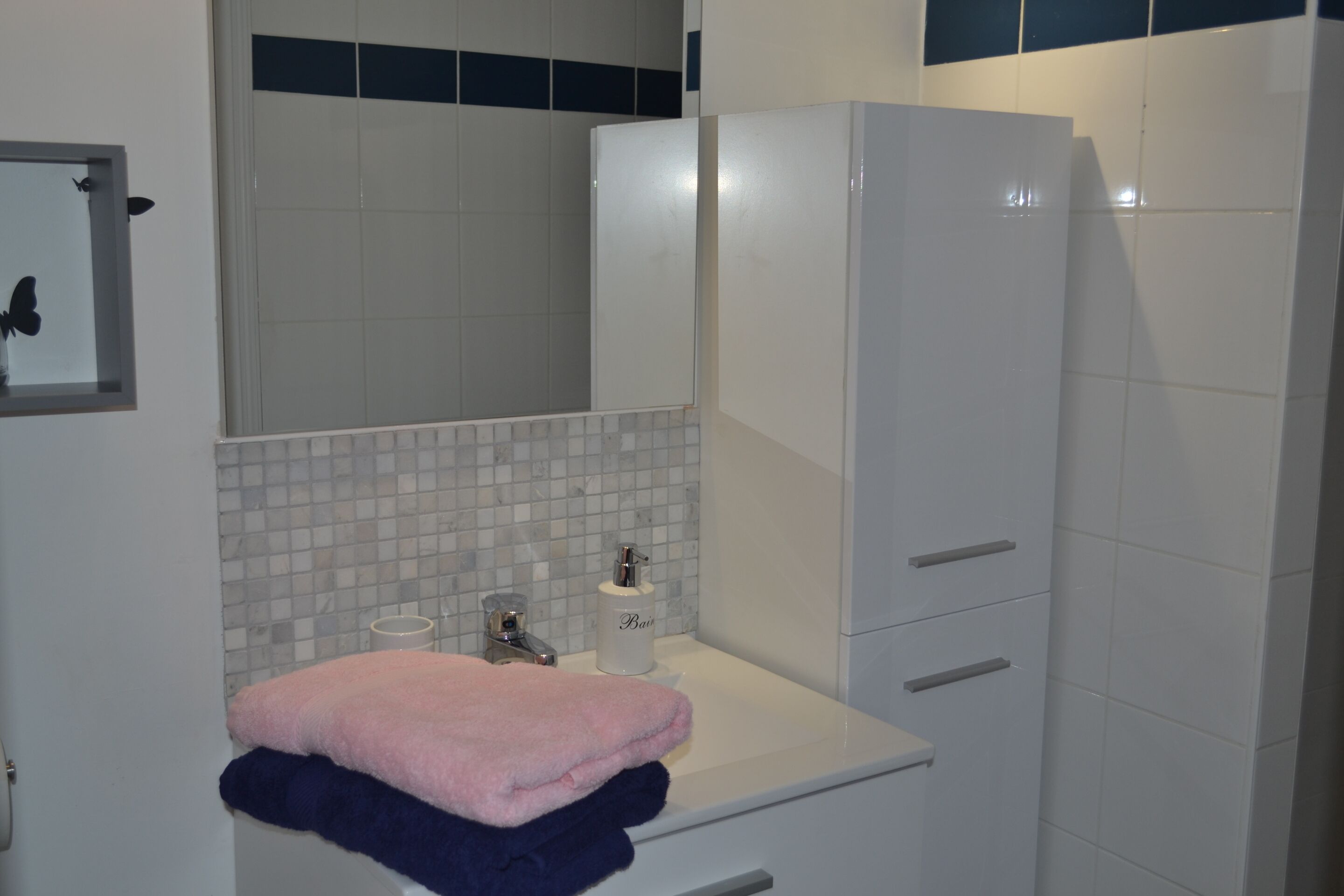 A bathroom with a white sink, a mirror, a towel rack, and a cabinet.