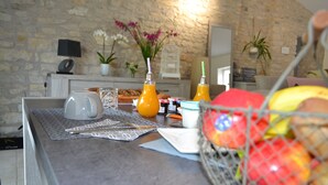 Una encimera de cocina con una cesta de fruta, dos botellas de jugo de naranja, una taza blanca y una pequeña planta en maceta.