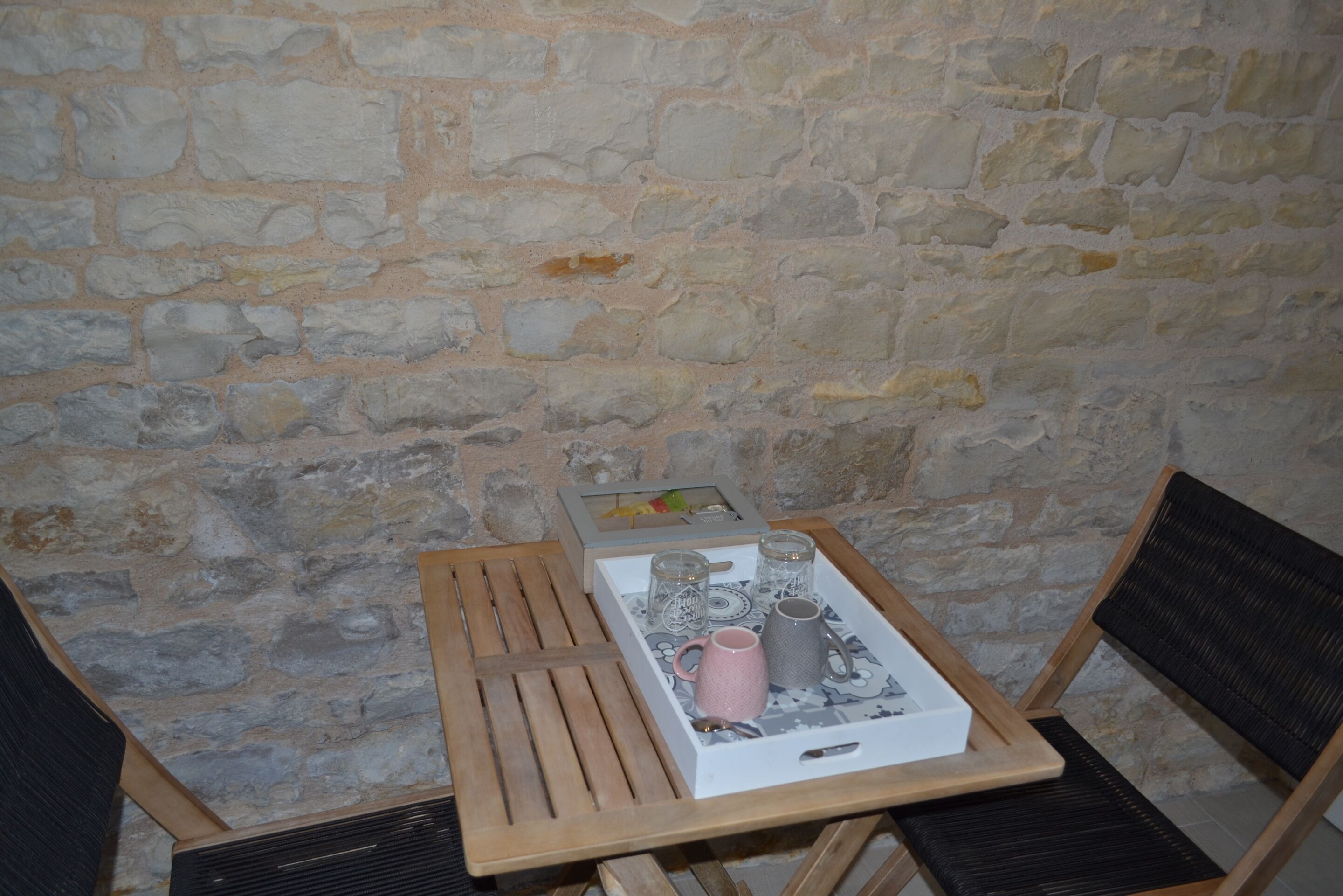 A stone wall, a wooden table with a tray, and two chairs.