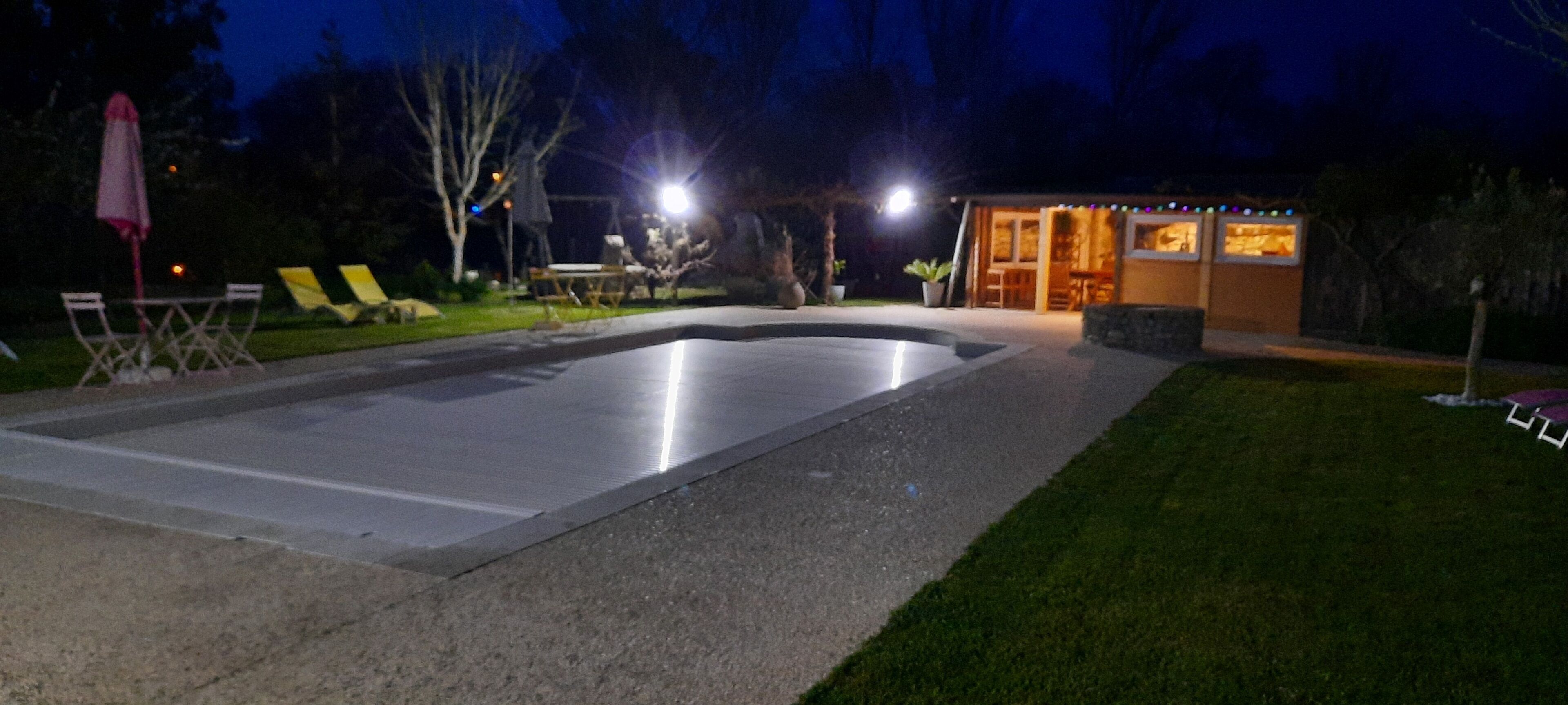 A swimming pool with a curved edge, surrounded by a grassy area and a small building with a glass door.