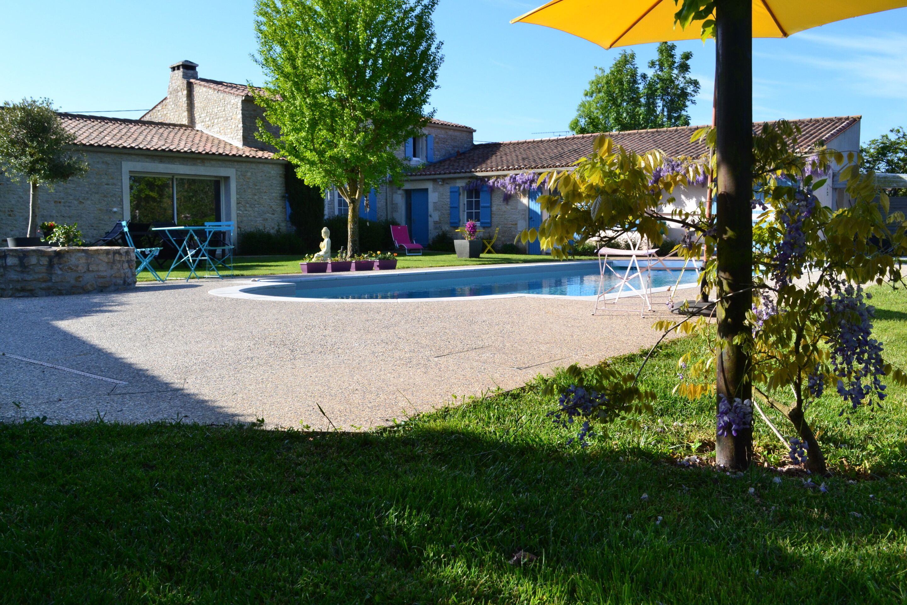 A house with a swimming pool, a patio with outdoor furniture, and a garden with trees and flowers.