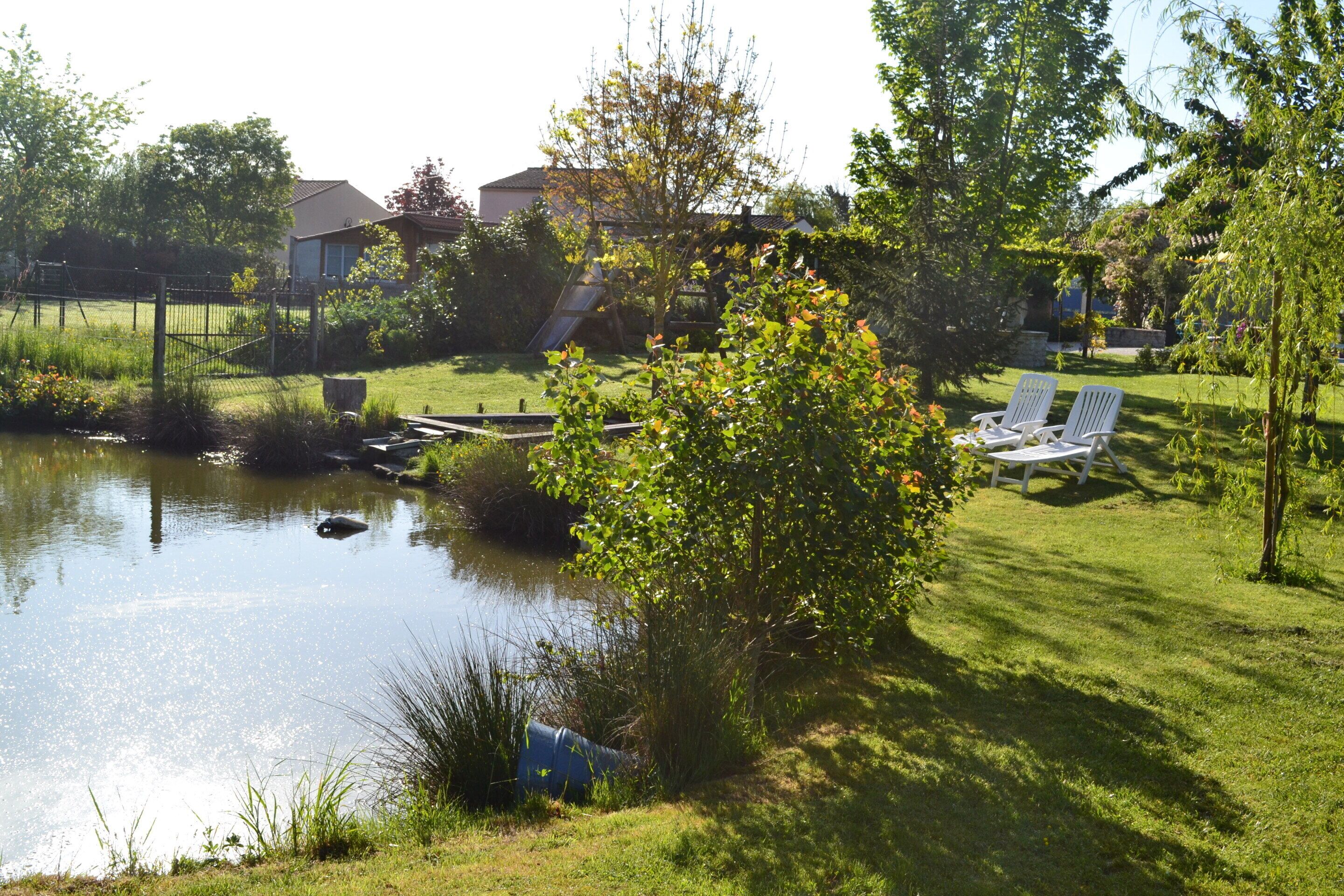 Ein ruhiger Garten mit Teich, einer Holzterrasse und einer Rasenfläche mit zwei weißen Liegestühlen.