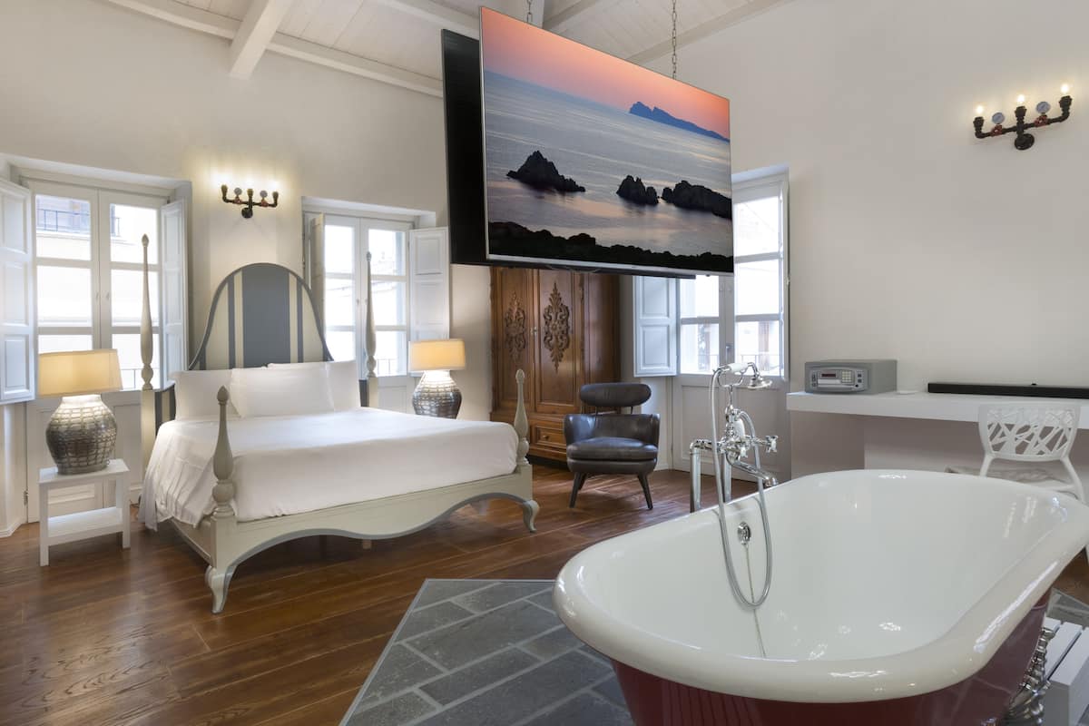 A bedroom with a large bed, a bathtub, and a TV mounted on the wall.