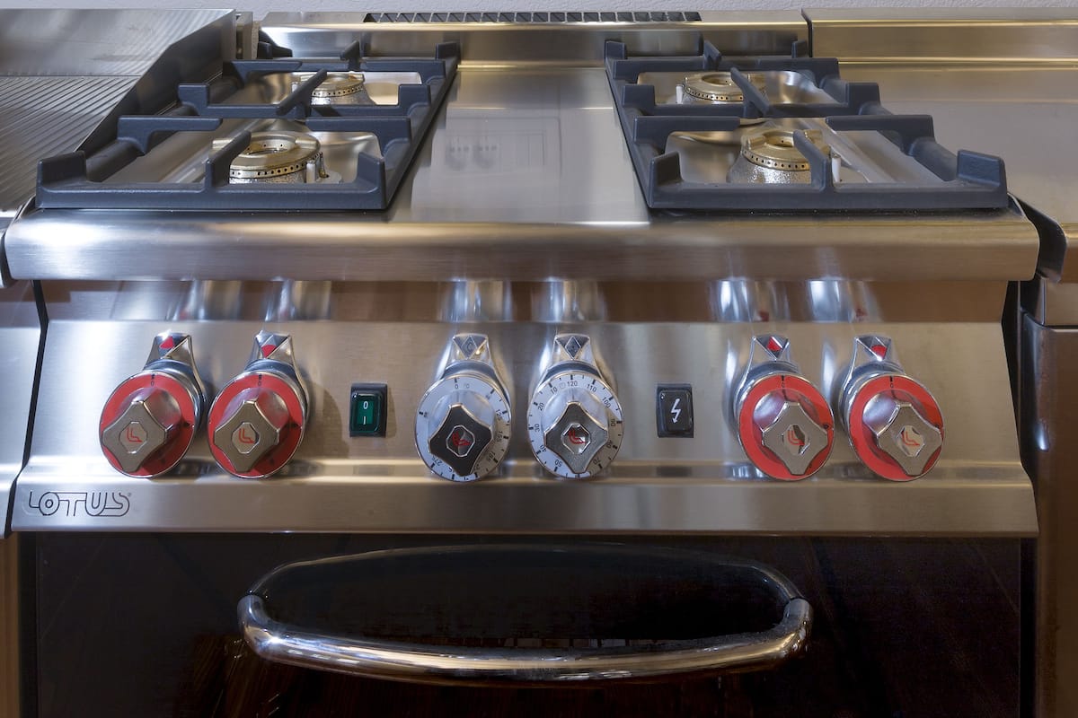 A kitchen with a gas stove, a black overhead light, and a stone wall background.