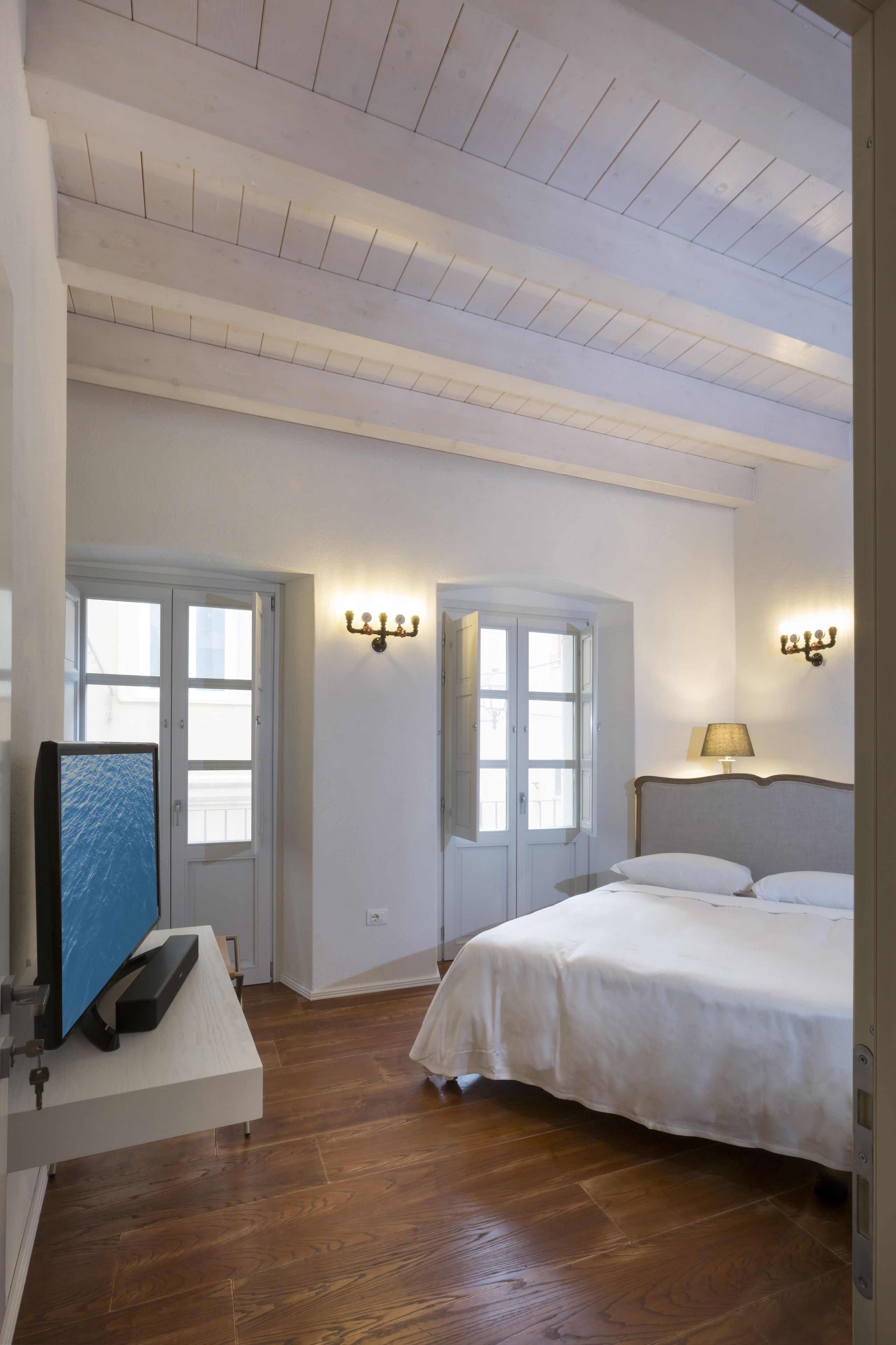 A bedroom with a bed, a desk with a computer, and two windows.
