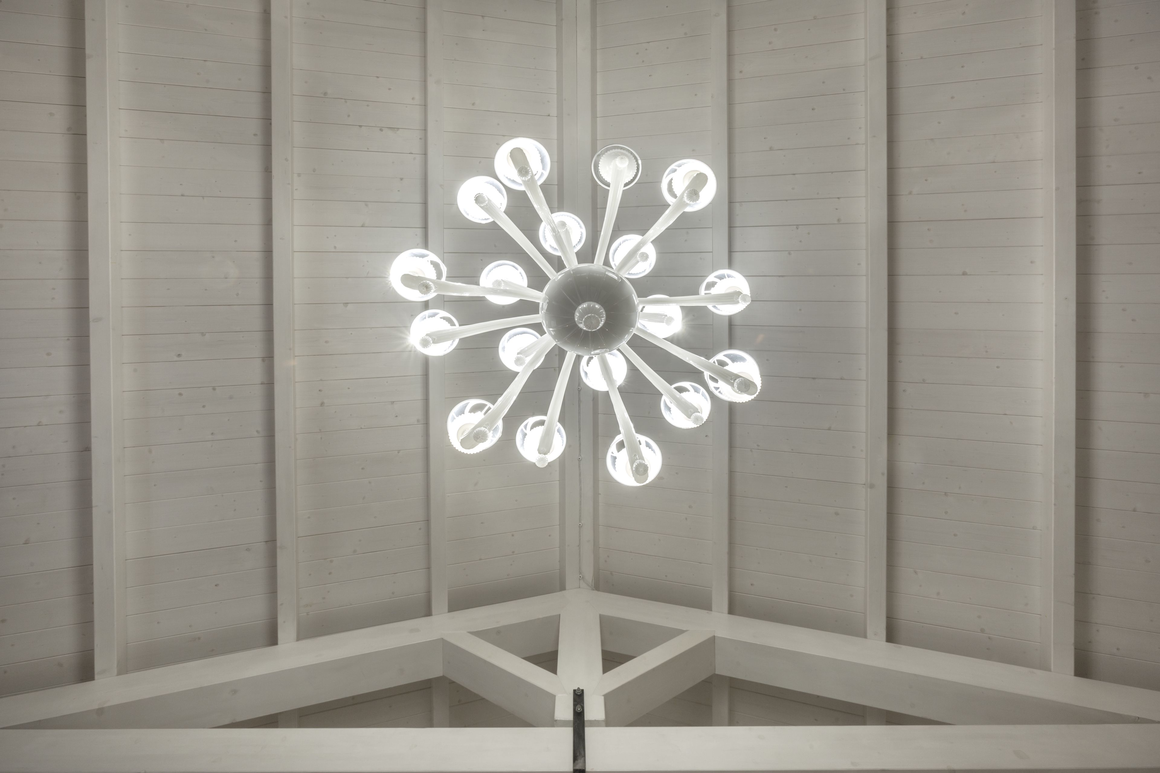 Un lustre moderne doté de plusieurs points lumineux, dans une pièce aux murs lambrissés et au plafond de couleur blanche.