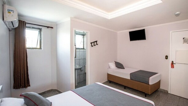 A hotel room with a bed, a TV, a bathroom, and a window.