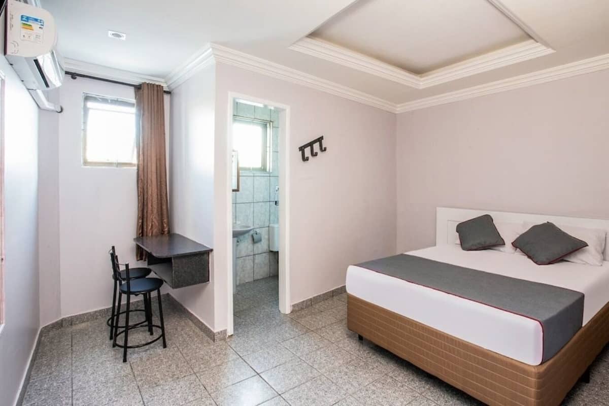 Un dormitorio con cama, escritorio y silla, baño visible a través de una puerta abierta y un ventilador de techo.