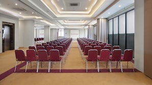 A conference room with rows of red chairs, a carpeted floor, and a modern ceiling design.