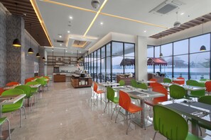 Un espace repas moderne avec de grandes fenêtres, une cuisine en arrière-plan et des chaises aux couleurs vives.