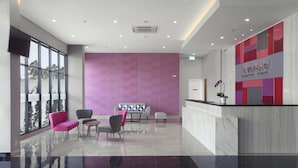 A modern reception area with a marble reception desk, a seating area with a sofa and chairs, and large windows offering a view of the outdoors.