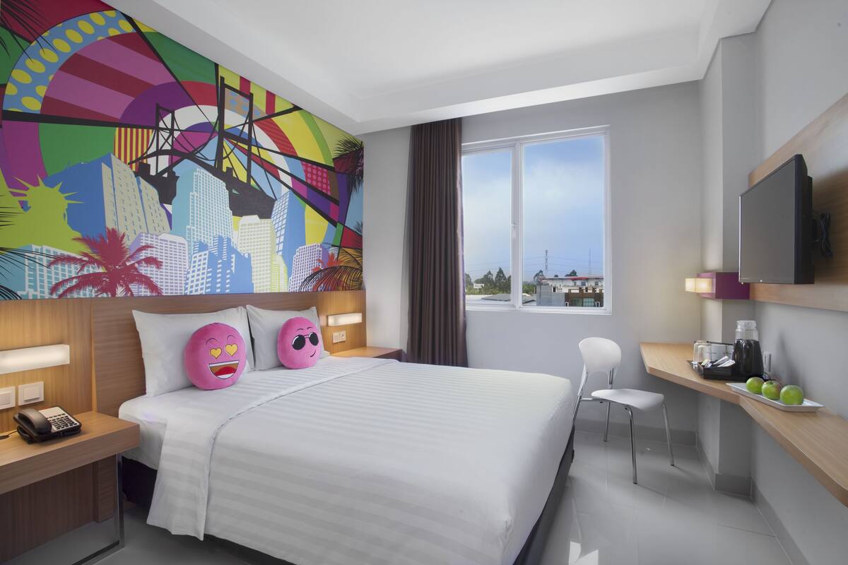 A hotel room with a bed, a desk, a chair, a TV, and a large window.