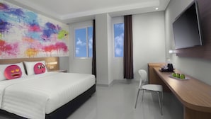 A modern hotel room with a large bed, a desk with a chair, a flat-screen TV, and a colorful abstract painting on the wall.