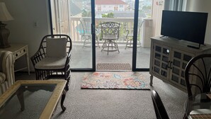 Un salon comprenant un téléviseur, un canapé, un fauteuil et une table. Il y a un balcon avec des chaises et une vue sur les immebles.