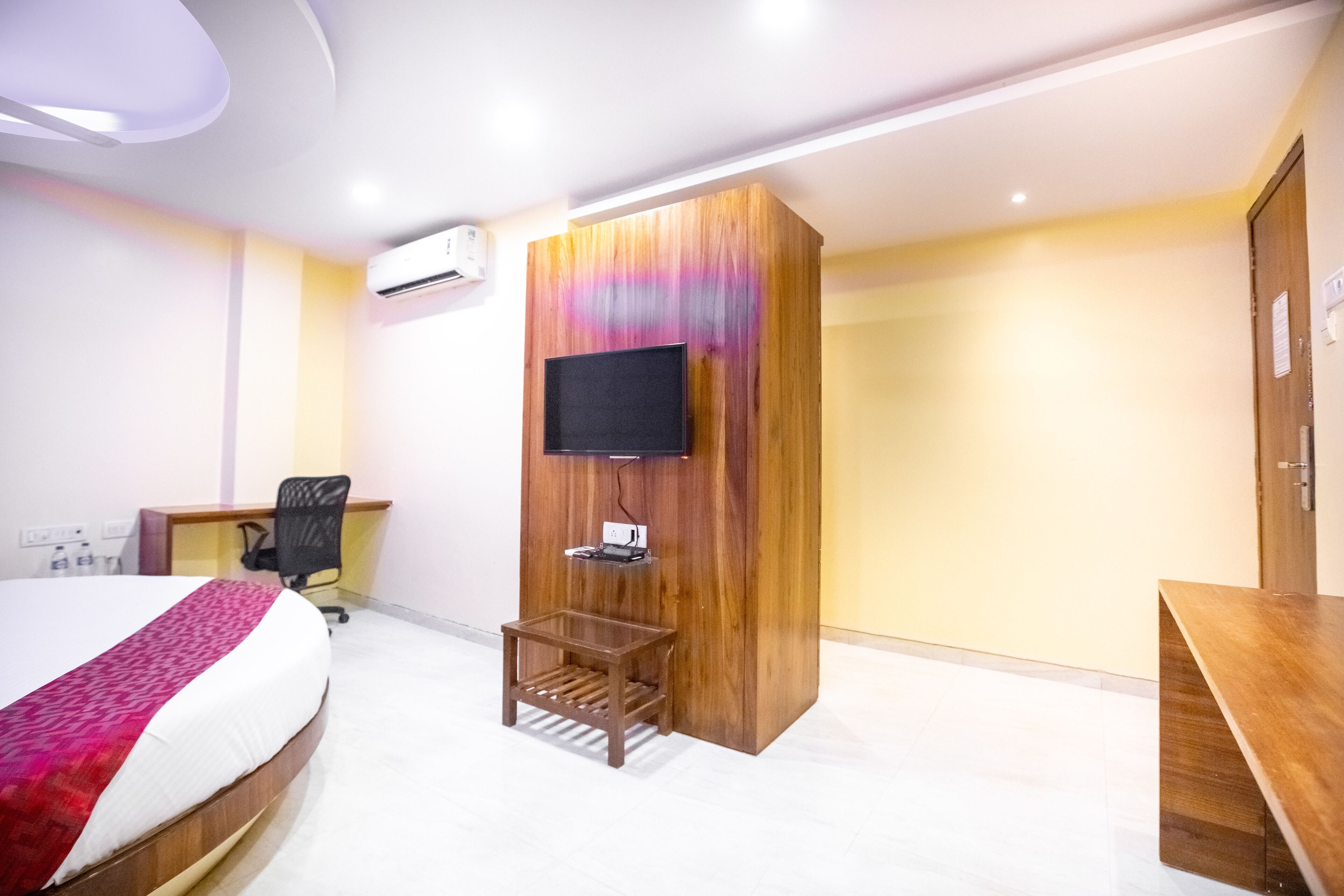A hotel room with a bed, a desk, a TV mounted on a wooden panel, and a small table.