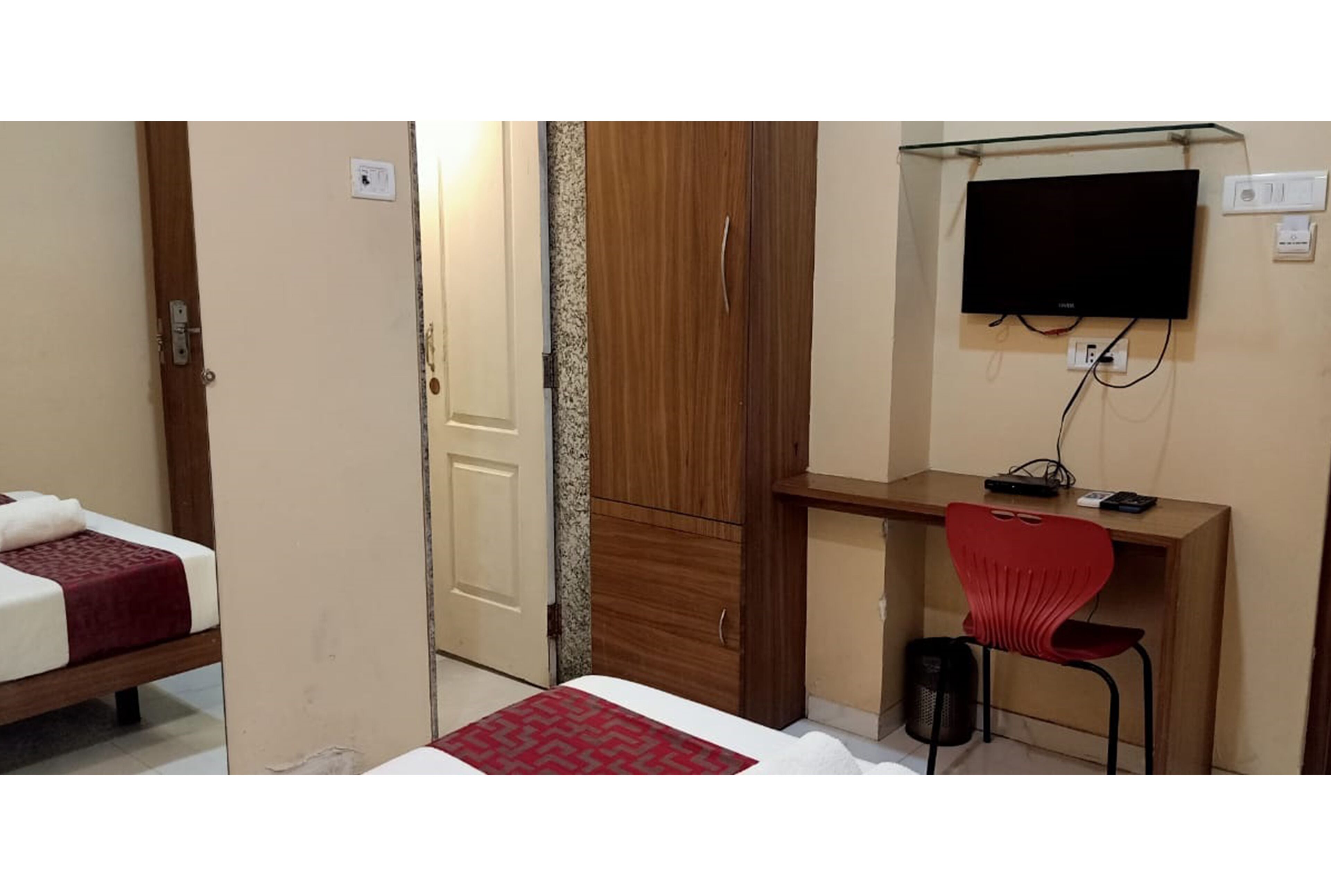 A hotel room with a bed, a desk with a chair, a television, and a wardrobe.