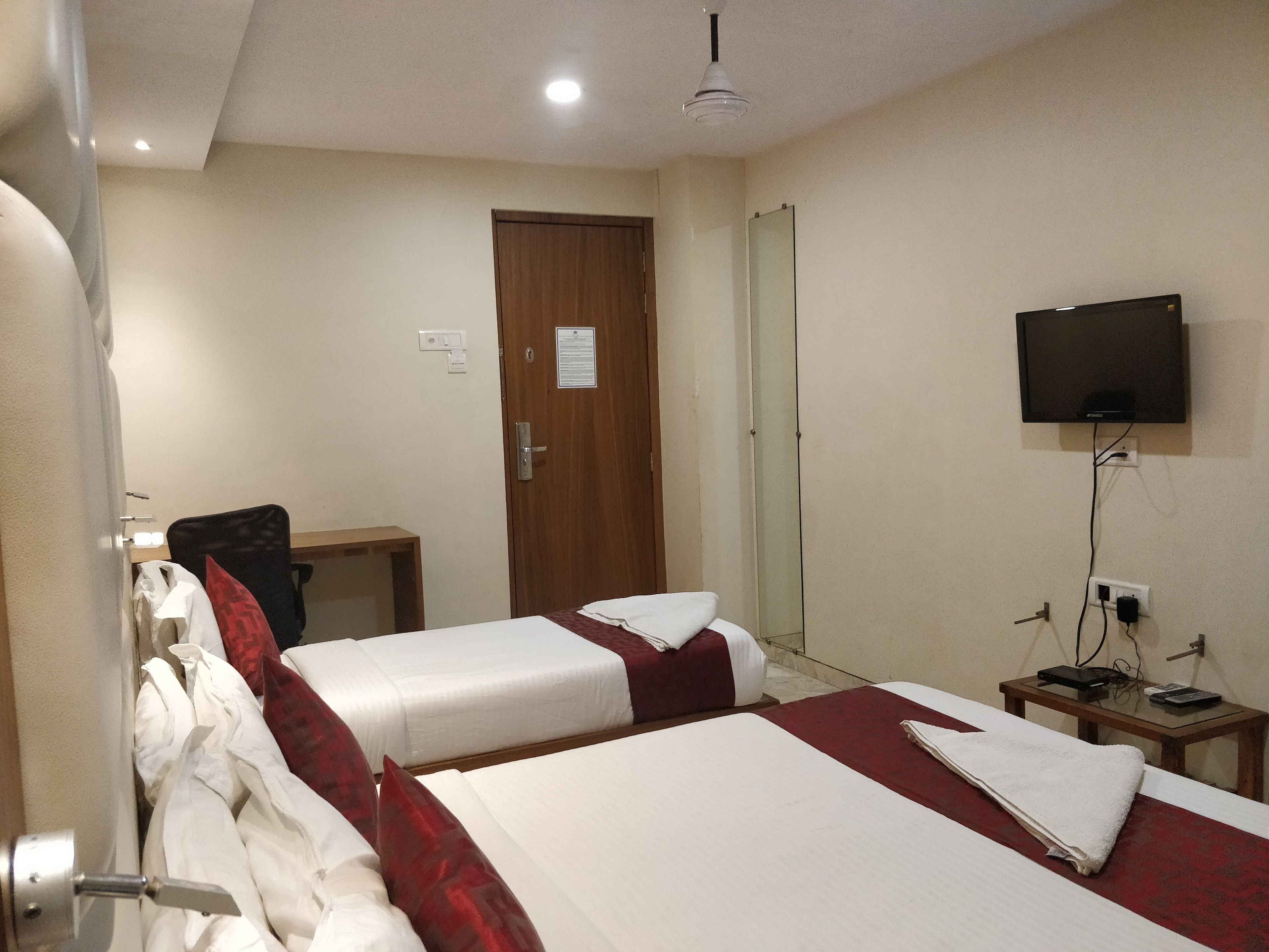 Una camera d'albergo con due letti, una scrivania, una sedia, una televisione e uno specchio.