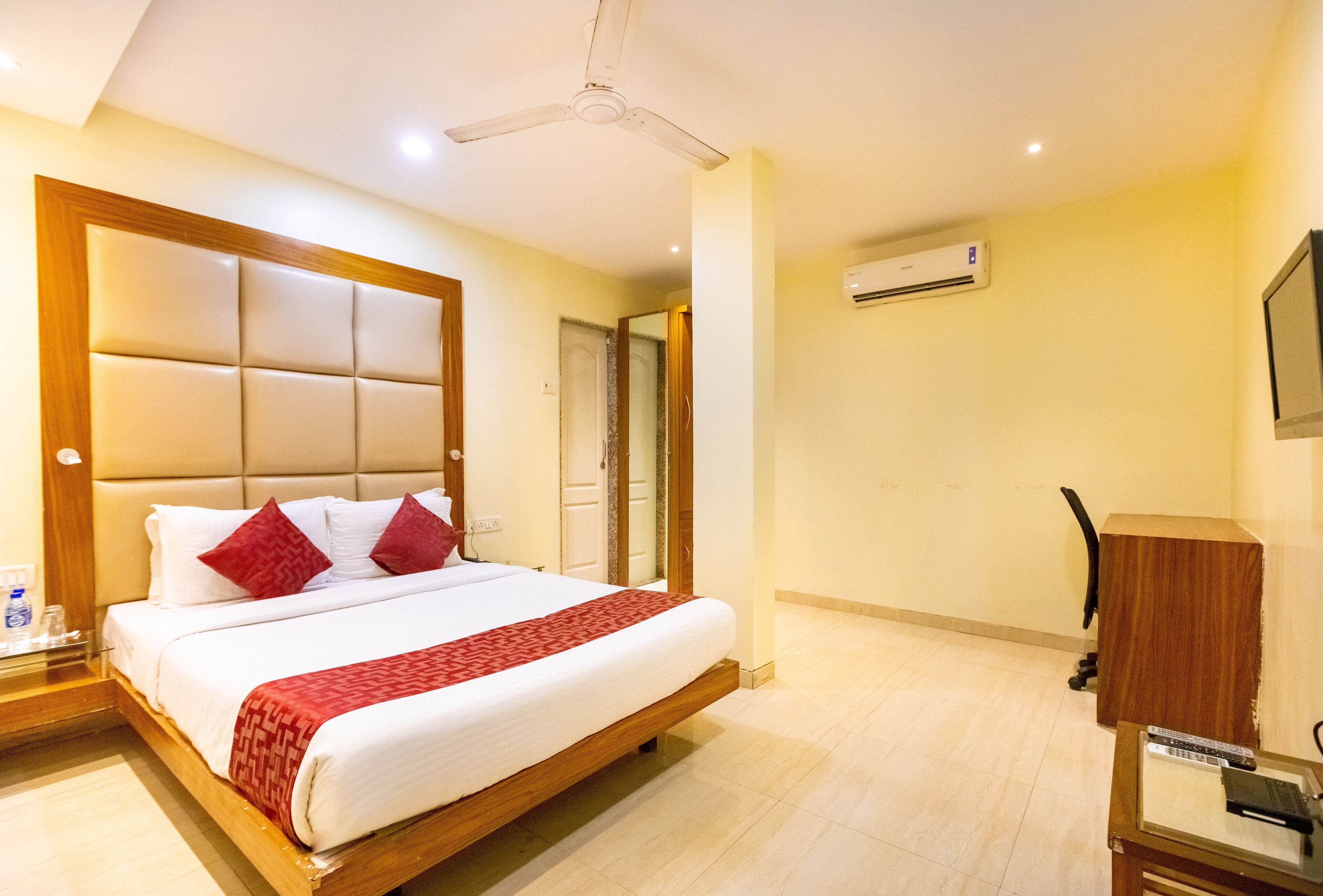 Quarto de hotel com uma cama grande, ventoinha no teto, ar condicionado e escrivaninha com cadeira.