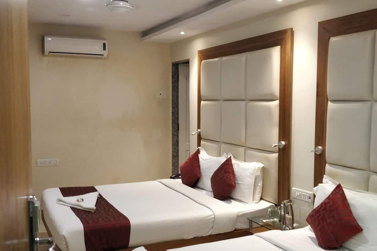 A hotel room with two beds, each with a headboard, a ceiling fan, and an air conditioning unit.