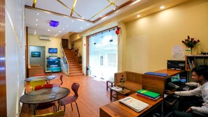 A modern hotel lobby with a wooden reception desk, a seating area with a sofa and chairs, a staircase, and a TV screen. - Hotel Apex International (Mumbai)