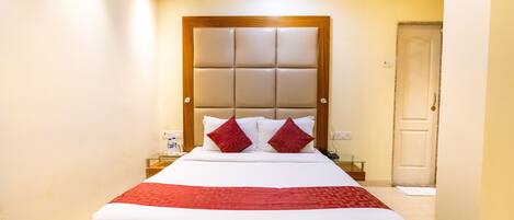 A hotel room with a large bed, a wooden headboard, and a bedside table with a glass top.