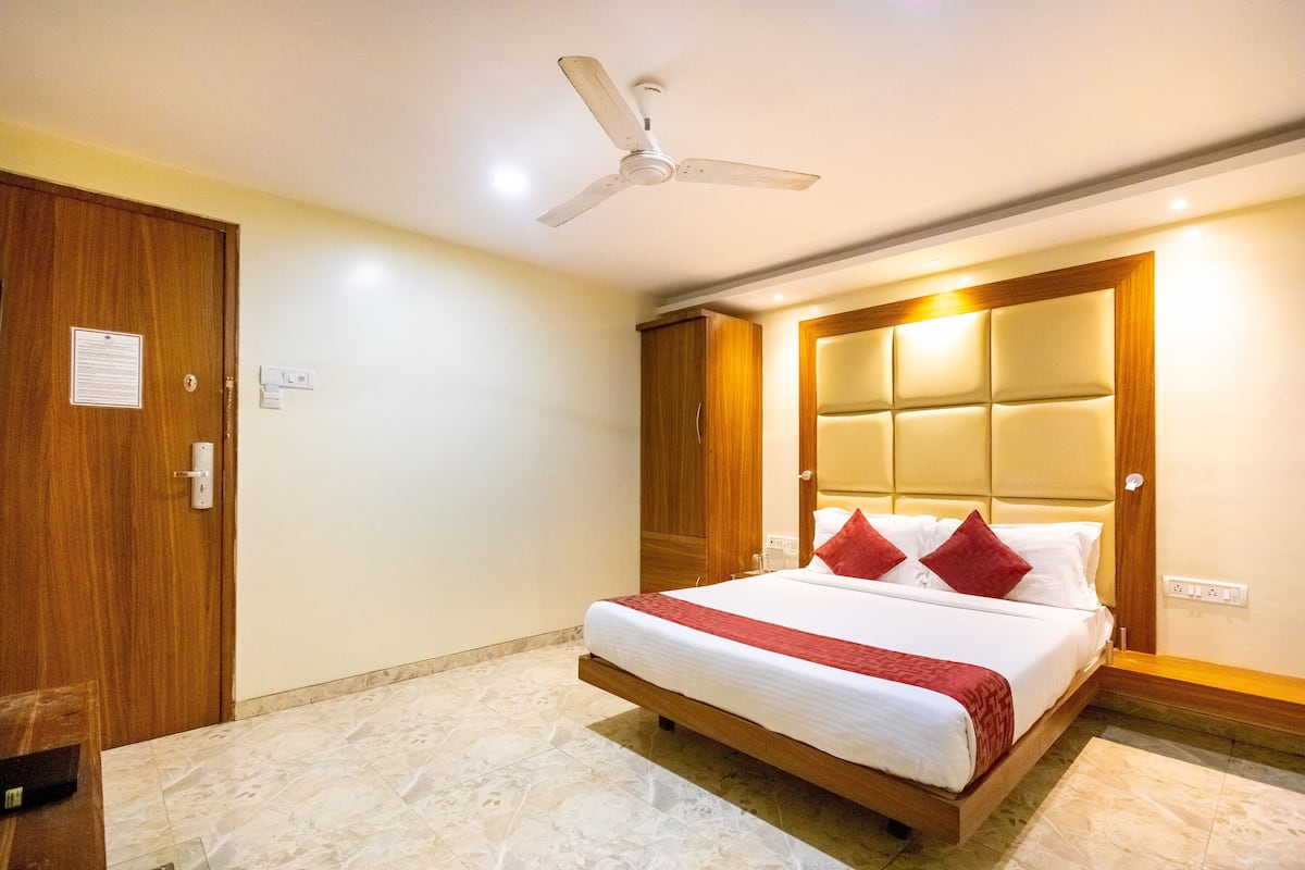 A bedroom with a bed, wooden wardrobe, ceiling fan, and a light switch on the wall.