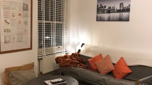 Un salon avec un canapé gris, des coussins orange et gris, une table basse ronde et un tapis à motifs.