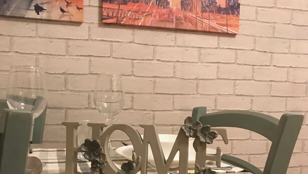 Une table à manger agrémentée d’un décor central représentant le mot « MAISON », une chaise avec un coussin marron et deux tableaux encadrés accrochés au mur.