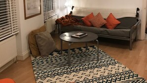 Un salon avec un canapé gris, des coussins orange à motifs, une petite table ronde et un tapis à motifs.