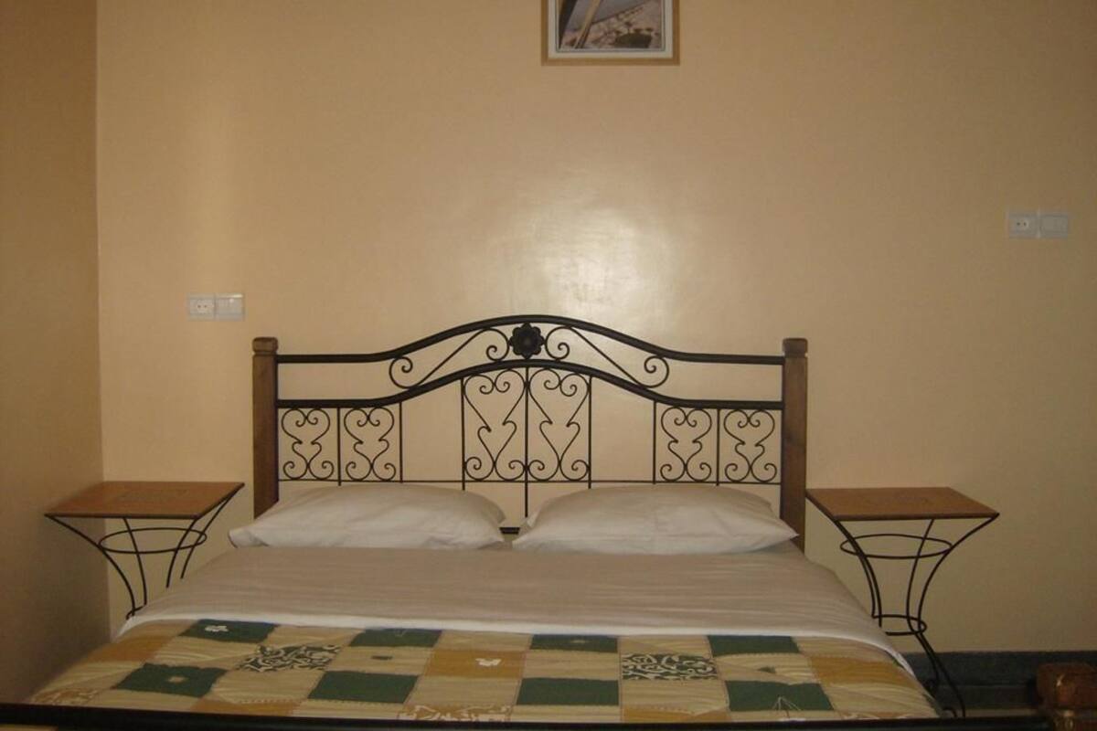 Uma cama com cabeceira de metal, duas mesas de cabeceira e um edredom.
