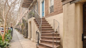 Une rangée de maisons de ville avec des escaliers extérieurs, un trottoir et des voitures garées.